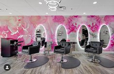 a salon with chairs and mirrors in front of a pink wall painted with flowers on it