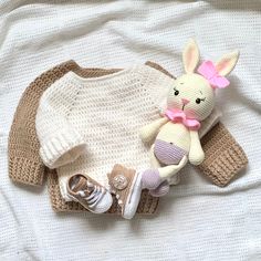 a knitted sweater and booties are laying next to a stuffed animal on a bed