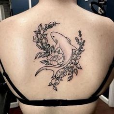 the back of a woman's shoulder with a fish and flowers tattoo on it