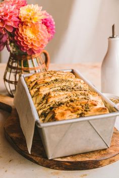 a loaf of bread sitting on top of a wooden cutting board next to a vase with flowers