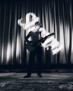 a man standing in front of a curtain playing a guitar