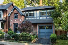 a brick house with two garages and trees in the front yard on a sunny day