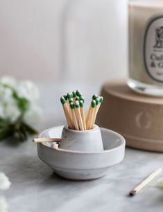 several matchsticks in a white cup on a marble table next to some flowers