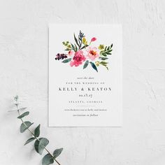 a wedding card with watercolor flowers and greenery on the front, next to a plant