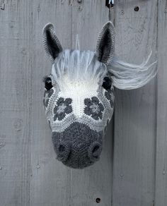 a knitted horse head hanging on a wooden fence