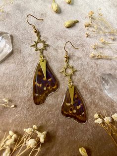 two brown and black butterfly shaped earrings sitting on top of a table next to dried flowers