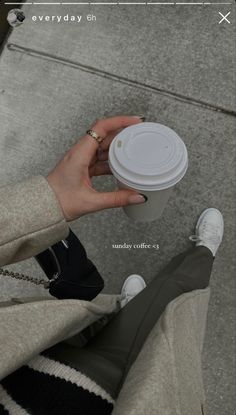 a woman is holding a cup of coffee on the sidewalk with her feet propped up