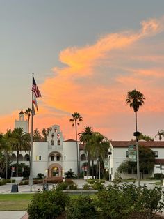 an american flag is flying in front of a white building with palm trees on the other side