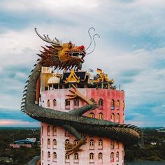 a large dragon statue sitting on top of a tall pink building next to a parking lot