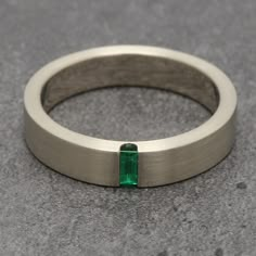 a close up of a ring with a green stone in it on a gray surface