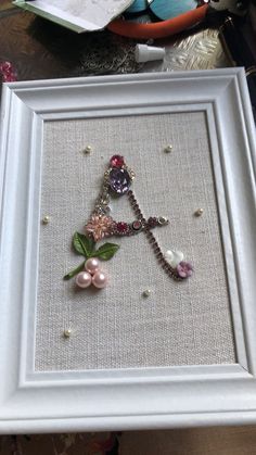 a white frame with some beads and flowers in it on a table next to other items