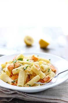 a white plate topped with pasta covered in cheese and sauce next to a fork on top of a napkin