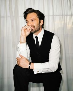 a man sitting in front of a curtain with his hand on his chin and looking at the camera