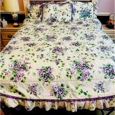 a bed with purple flowers and green leaves on the comforter, along with two night stands