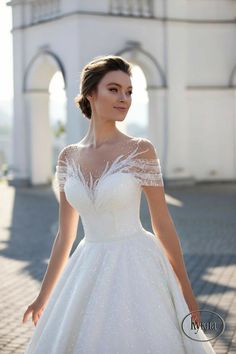 a woman in a white wedding dress standing on a brick walkway with her hands behind her back