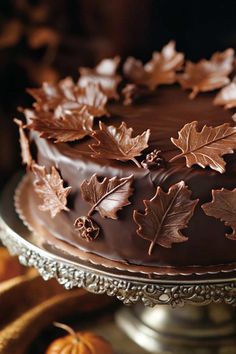 a chocolate cake decorated with leaves and acorns sits on a silver platter