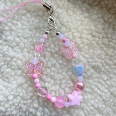 a pink bracelet with butterfly charms and beads on a white blanket, next to a keychain