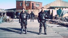 two men in scuba suits standing on a dock