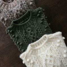 three knitted sweaters sitting on top of a wooden floor next to each other