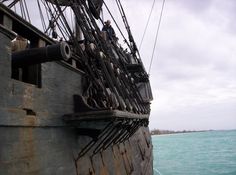 an old sailing ship in the middle of the ocean with people on it's side