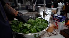 a person in black gloves is washing spinach leaves on a kitchen counter with other ingredients and utensils