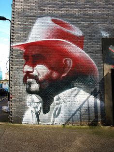 a mural on the side of a building with a man wearing a red cowboy hat