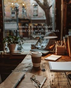 a cup of coffee sitting on top of a wooden table next to a notebook and pen