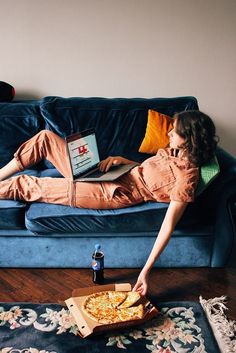 a person laying on a couch with a pizza in front of them and a laptop