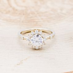 a white gold ring with an oval cut diamond surrounded by smaller round diamonds on a wooden surface