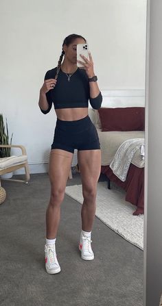 a woman taking a selfie with her cell phone in front of a mirror wearing shorts and sneakers