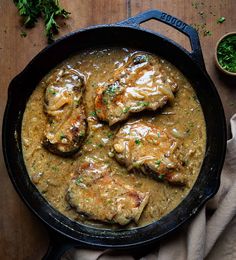 some meat and gravy in a skillet on a wooden table with parsley