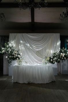 a table with white flowers and candles on it in front of a curtained wall