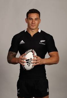 a man holding a rugby ball and posing for a photo in front of a gray background