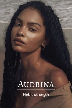 a woman with long black hair sitting on the beach looking off into the distance while wearing gold hoop earrings