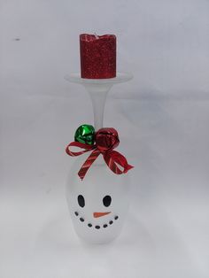 a glass candle holder with a snowman face and red ribbon on it's head