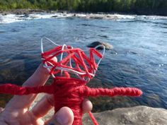 someone is holding up a piece of red string next to a river with rocks and trees in the background