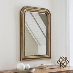 a mirror sitting on top of a wooden table next to a vase and two eggs