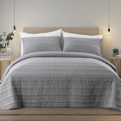 a bed with grey bedspread and pillows on top of it in a room