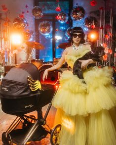 a woman in a yellow dress is holding a dog and sitting next to a stroller