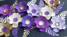 purple and white paper flowers are arranged on a black background with gold leaves, branches and foliage