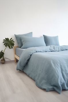 a bed with blue sheets and pillows next to a potted plant on the floor