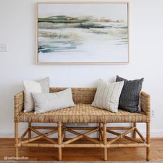 a wicker bench with pillows on it in front of a painting