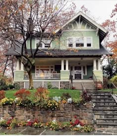 a green house with flowers and trees in the front yard on a cloudy fall day