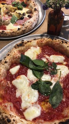 two pizzas sitting on top of metal pans covered in sauce and toppings