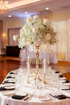 an elegant centerpiece with white flowers and greenery sits on a table at a wedding reception