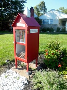 a red mailbox sitting in the middle of a flower bed next to a house