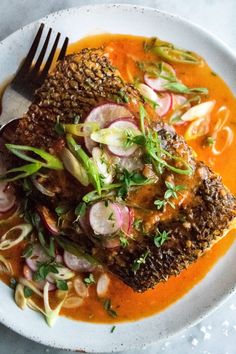 a white plate topped with fish covered in sauce and garnished with veggies