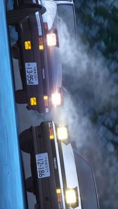 two cars parked next to each other in front of a blue wall with clouds and trees