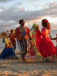 some people are dancing on the beach at sunset