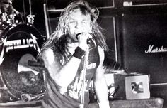 a man with long hair holding a microphone in front of his face while standing on stage